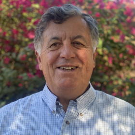 Photo of Phil Alonso wearing a blue shirt in front of a hedge with pink flowers