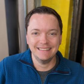 JD Leonard smaling in front of a yellow background